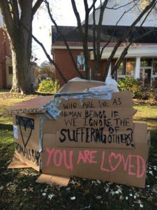 Painting on the cardboard structure reads:"Who are we as human beings if we ignore the suffering of others? You are Loved" Photo by Mariah Pasinski.